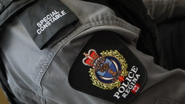 The Regina Police Service arrested 33 year-old Douglas Ramos Fundao for sexual assault, sexual interference, and invitation to sexual touching. A badge shows the logo of the Regina Police Service and the phrase "Police Regina." Another shoulder patch indicates the officer is a special constable.
