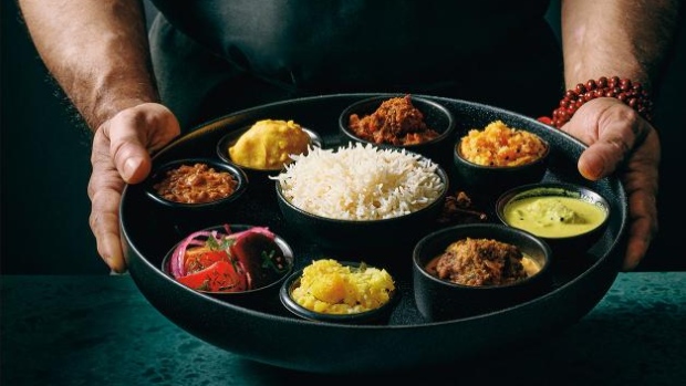 Chef Joe Thottungal on creating the perfect thali in his new cookbook; A person holds a plate with rice in the middle and several colourful foods around it\.