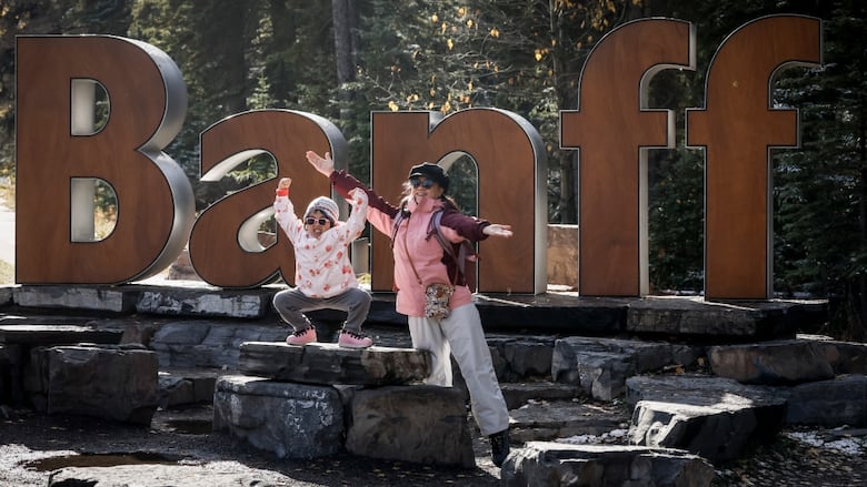 Two young tourists pose for a picture on a Banff sign.