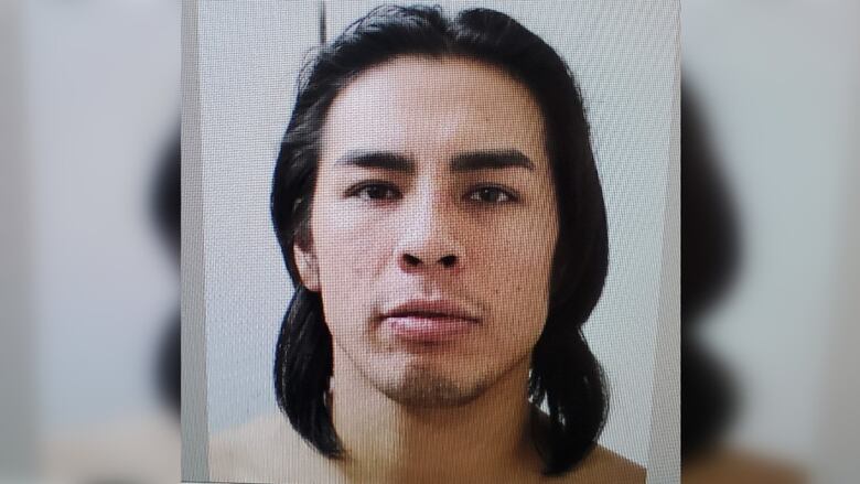 Mug shot of man with long black hair, showing his head and top of shoulders,