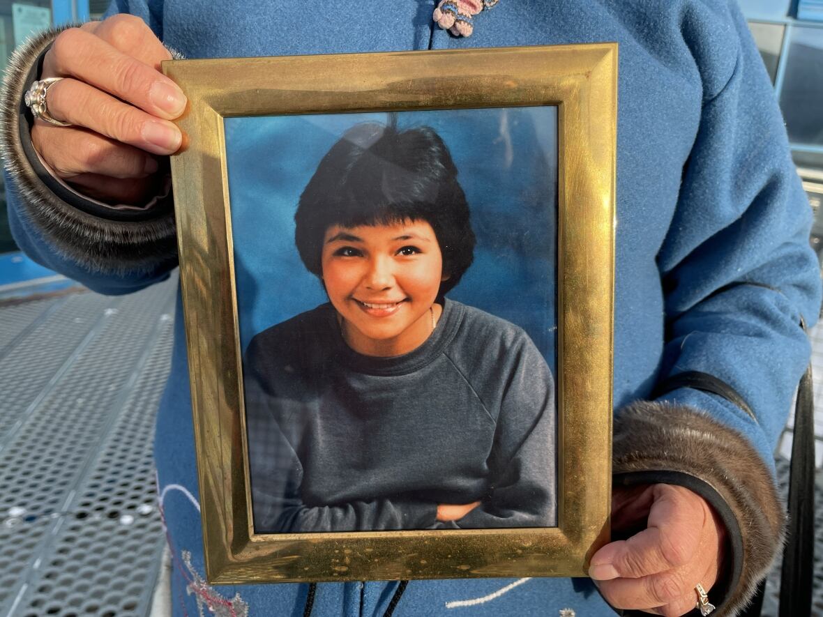 A framed photograph of a young girl, held by her sister 