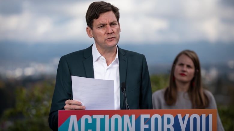 A man delivers a news conference at a podium marked 'Action For You', as a woman looks on.