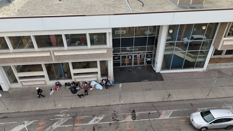 People sleep and squat outside of a city building.