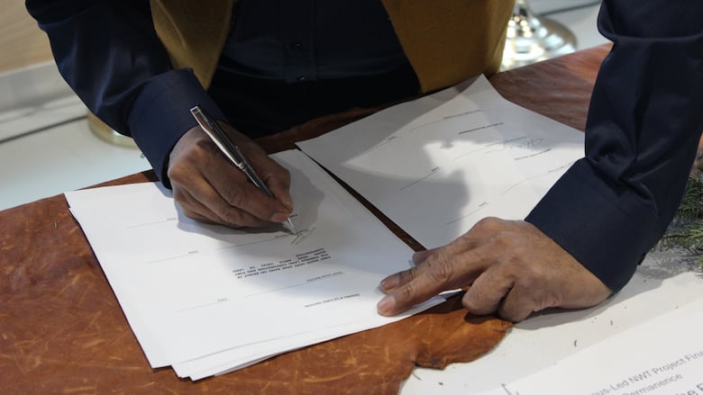 Close up of hands signing a document on a table.