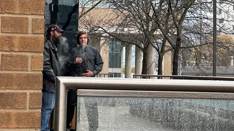 A man stands outside smoking beside another man.