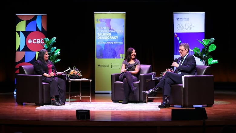 Three people sitting on stage talking into microphones.