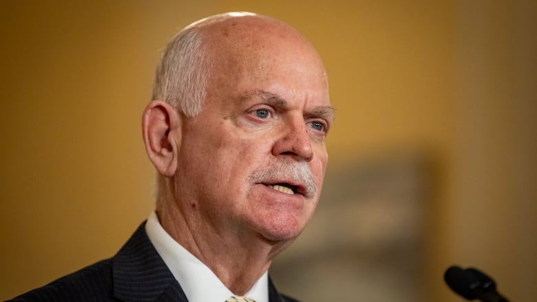 A man with balding white hair speaks into a mic.