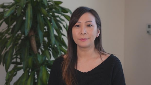 An East Asian woman sits in front of a plant.