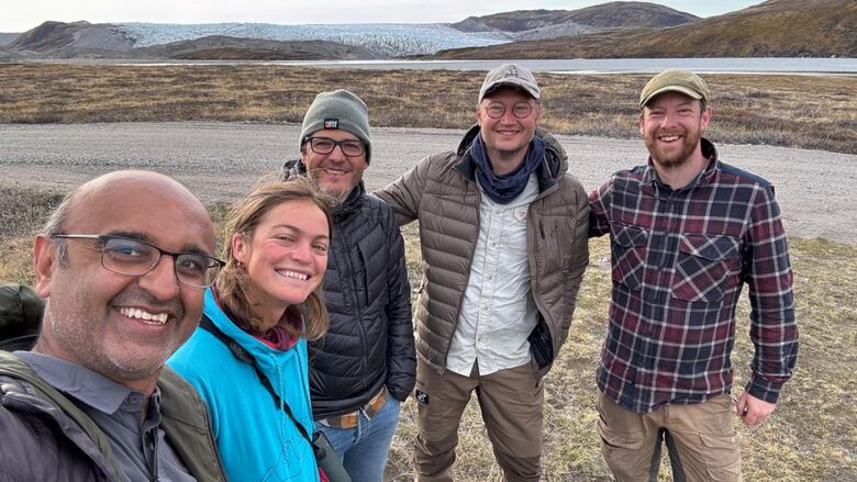 A group of five people taking a selfie with a road and a glacier in the background.