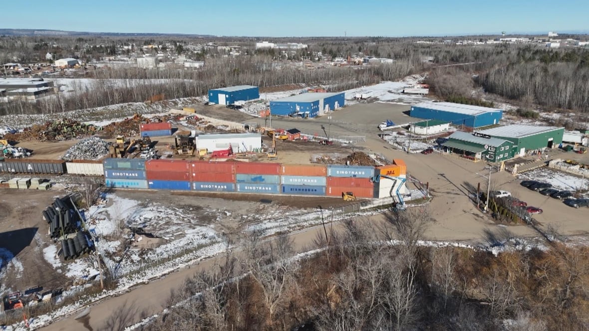 A drone view of a scrapyard with a colourful wall of shipping containers around part of the site.