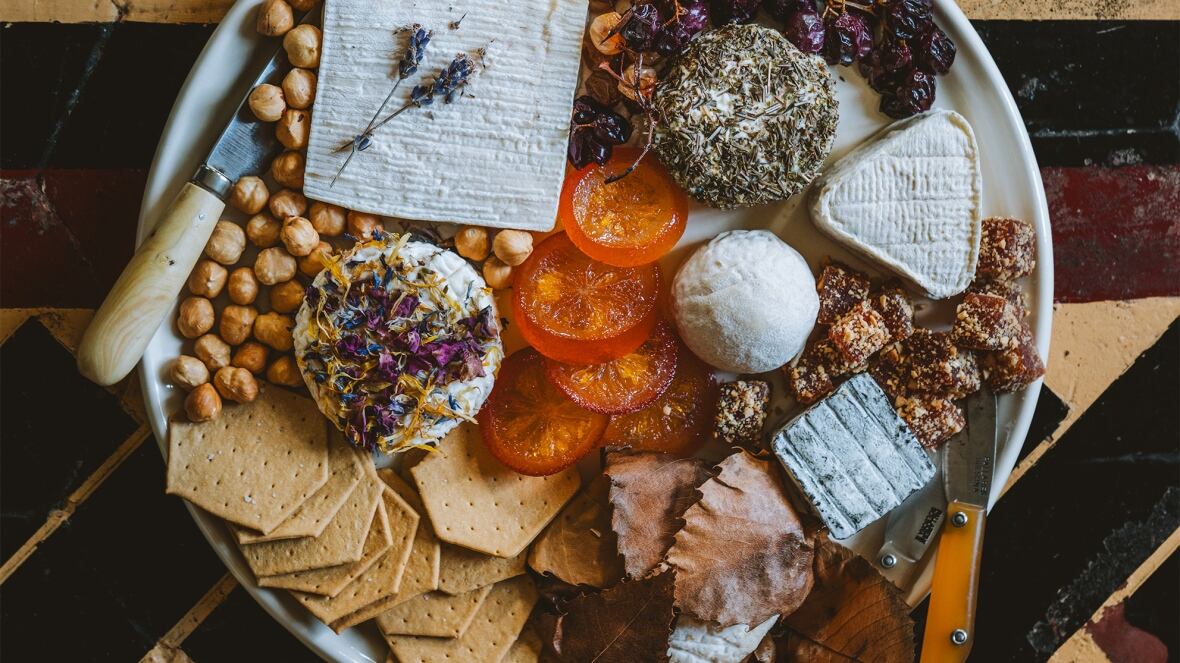 Overhead shot of a plate with multiple types of cheese, roasted grapes, hazelnuts and apricots. 