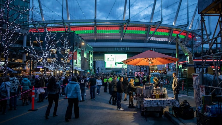 Groups of people mill around booths outside a stadium.