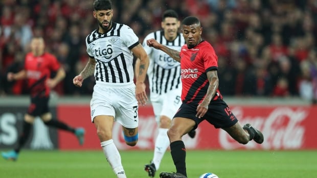 Two male soccer players battle for ball.