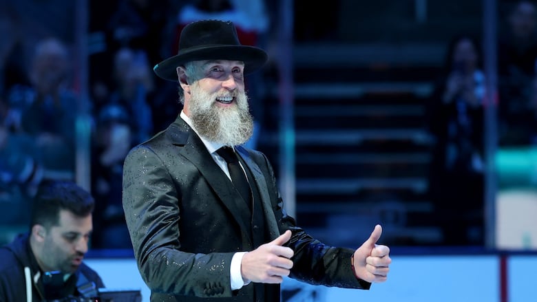 Adult male in suit gives thumbs up.