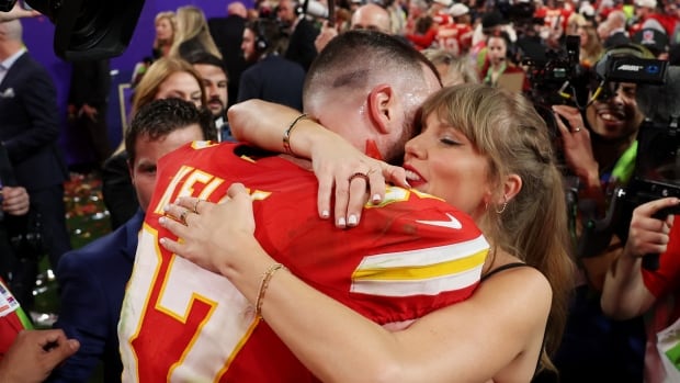 A male football player without his helmet on hugs a woman as media members take pictures.