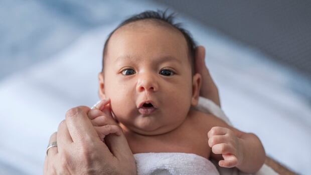 Close up photo of a one week old baby boy with dark hair and eyes open.