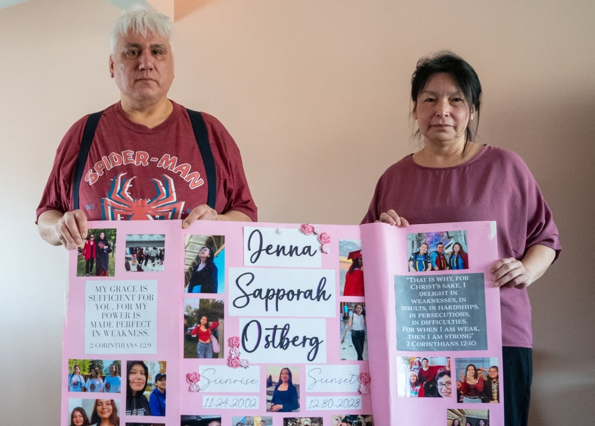 Two people stand in a room, holding a poster.