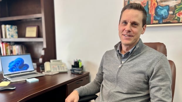 Rob Lantz sits at his desk wearing a collared shirt and a grey zip up sweater.
