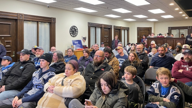 Charlottetown Privateers optimistic about new turf fields following committee meeting; People sit in chairs all facing the same direction\. The room is packed full so some are left to stand\. Some a wearing grey and blue jerseys\. 