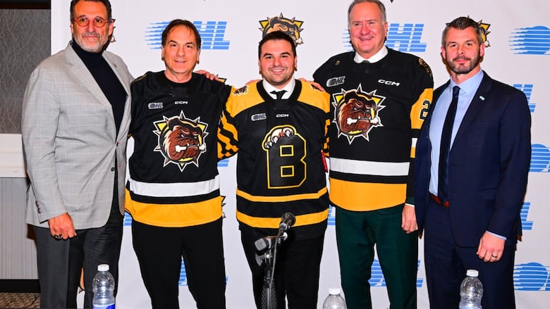 Five men, including three in Bulldogs jerseys, stand and smile.