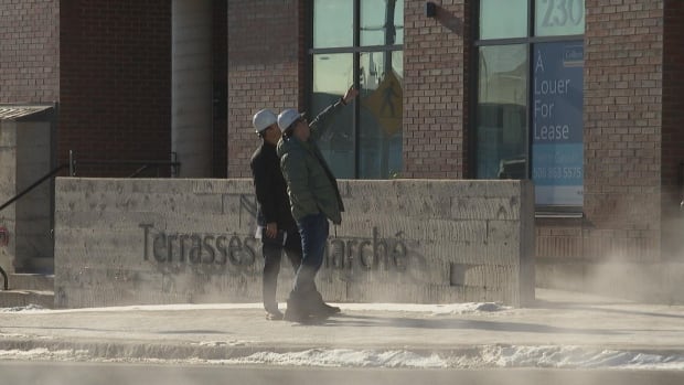 Two people outside 230 Champlain St. in Dieppe on Jan. 17, 2025, gesturing at the structure from the sidewalk. Two men in white hardhats on the sidewalk.