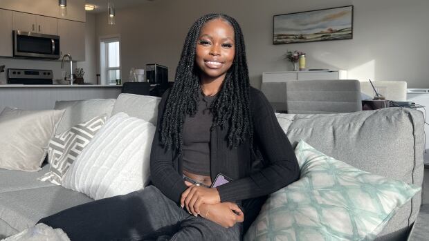 A woman dressed in black sits on a light grey couch.