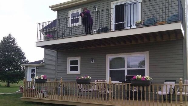 Linda MacCallum stands on the patio of the family home in Marshfield, P.E.I. A fire two days after Christmas in 2024 destroyed the house. A woman stands on the veranda at the back of a two-storey house.