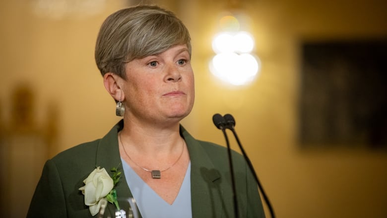 A white woman with short hair and hooped earrings speaks to a mic.