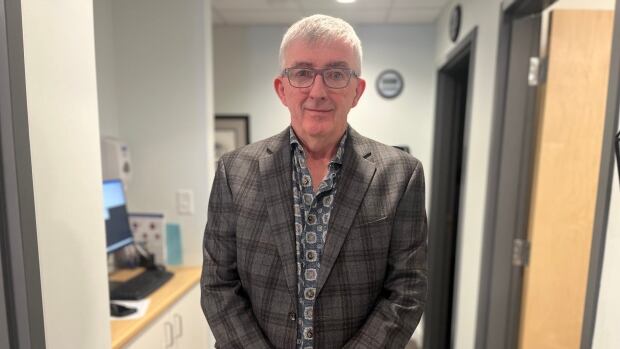 Guy Boswall stands in the doorway wearing a checkered suit jacket and patterned shirt.