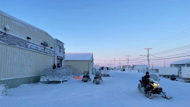 A resident passing on a snowmobile near the Northern Store in Sanirajak, Nunavut, on Jan. 18, 2025. A rush of Arctic air plunged parts of North America into bitter cold starting this weekend. In parts of Nunavut, Environment Canada said, it could feel as cold as –58 C over the coming days. A resident leaving on a snowmobile outside XX in Sanirajak, Nunavut.
