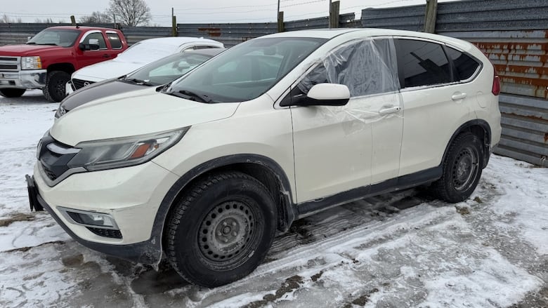 A white Honda CR-V SUV with a broken window parked in a lot. The broken window is covered over with plastic.