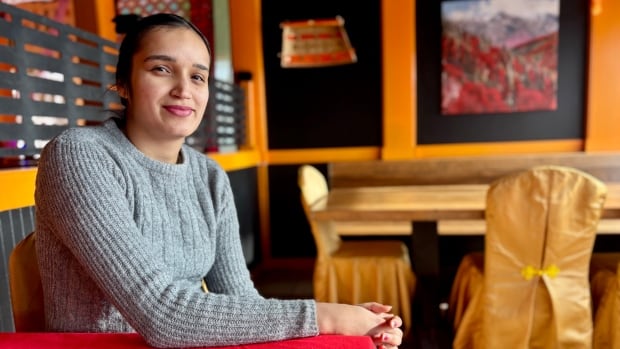 Harneet Brar sits at a table in her restaurant which is covered with a red table cloth. The chairs at the tables have gold covers on them.