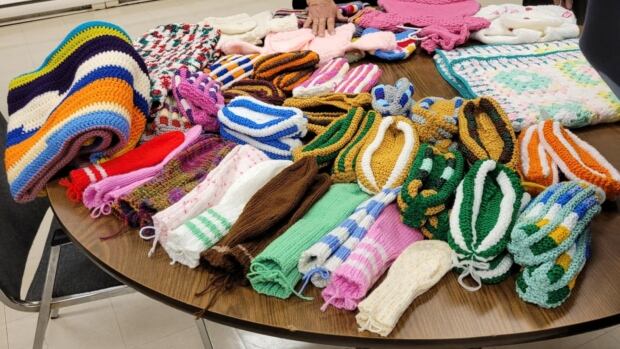 The group of 25 knitters based in the Shediac region, knit and crochet enough warm clothes and blankets to help 400 families in need each year. hand-knitted mittens, scarves and blankets displayed on a table.