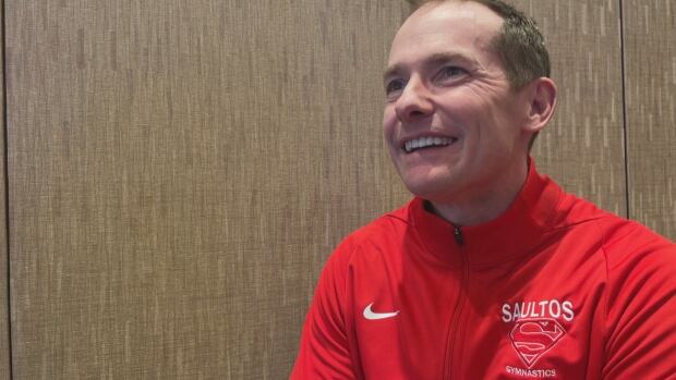 Gymnast Scott Chandler says he's trying to qualify for a national competition at age 49. A man in a red jacket smiling and not looking at the camera.
