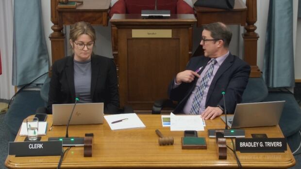 A woman and a man seated at a table, with laptops and papers in front of them