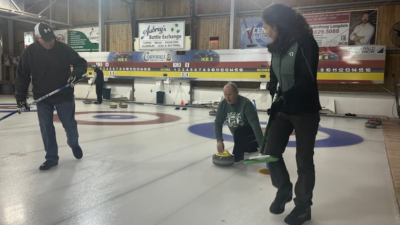 Three individuals engaged in a game of curling on a curling rink