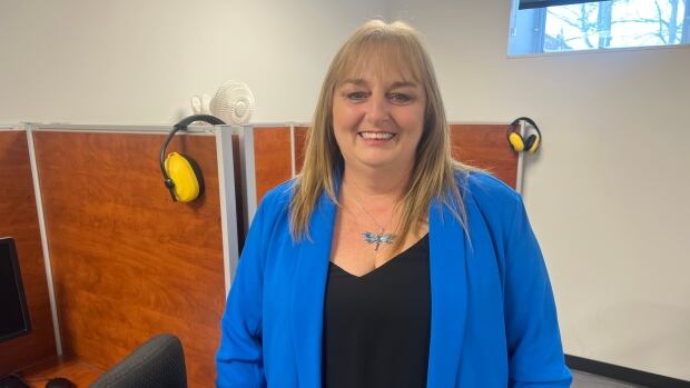 Sandra Griffin wears a black shirt under a blue blazer and a dragonfly necklace as she smiles at the camera.