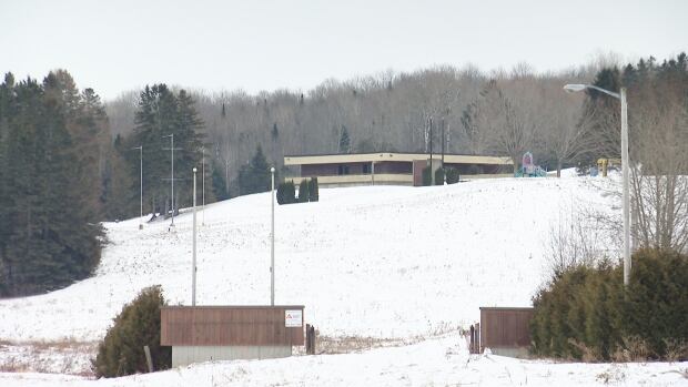 xxx An oblong brown building with light wood accents sits in a snowy field.