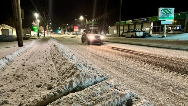 A snow-covered street early morning, with streetlights, with a car driving