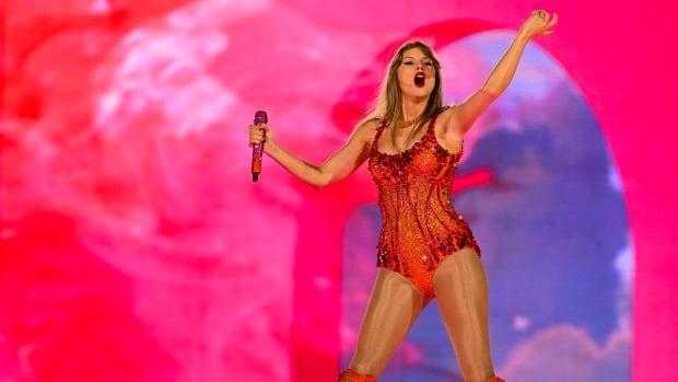 Taylor Swift stands on stage, wearing a red sequin onesie.