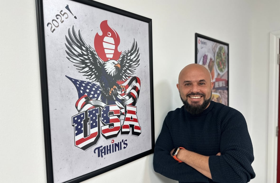 Omar Hamam, el propietario de Tahini's, se encuentra frente a un cartel que muestra el nombre del restaurante y las palabras USA y un águila calva gigante.