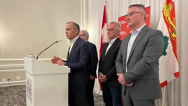 Federal Liberal leadership candidate Mark Carney speaks at a podium with P.E.I. MPs Lawrence MacAualay, Sean Casey and Heath MacDonald behind him at the Rodd Charlottetown on Saturday, Feb. 1, 2024. A man speaks at a podium with three others standing behind him in a hotel ballroom.