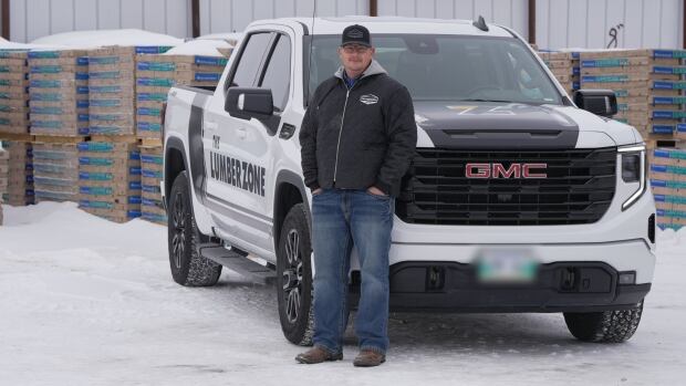 A man stands beside a truck in a lumber yard.
