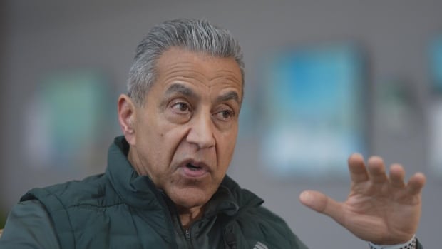 A South Asian man with white hair is seen gesturing as he speaks.