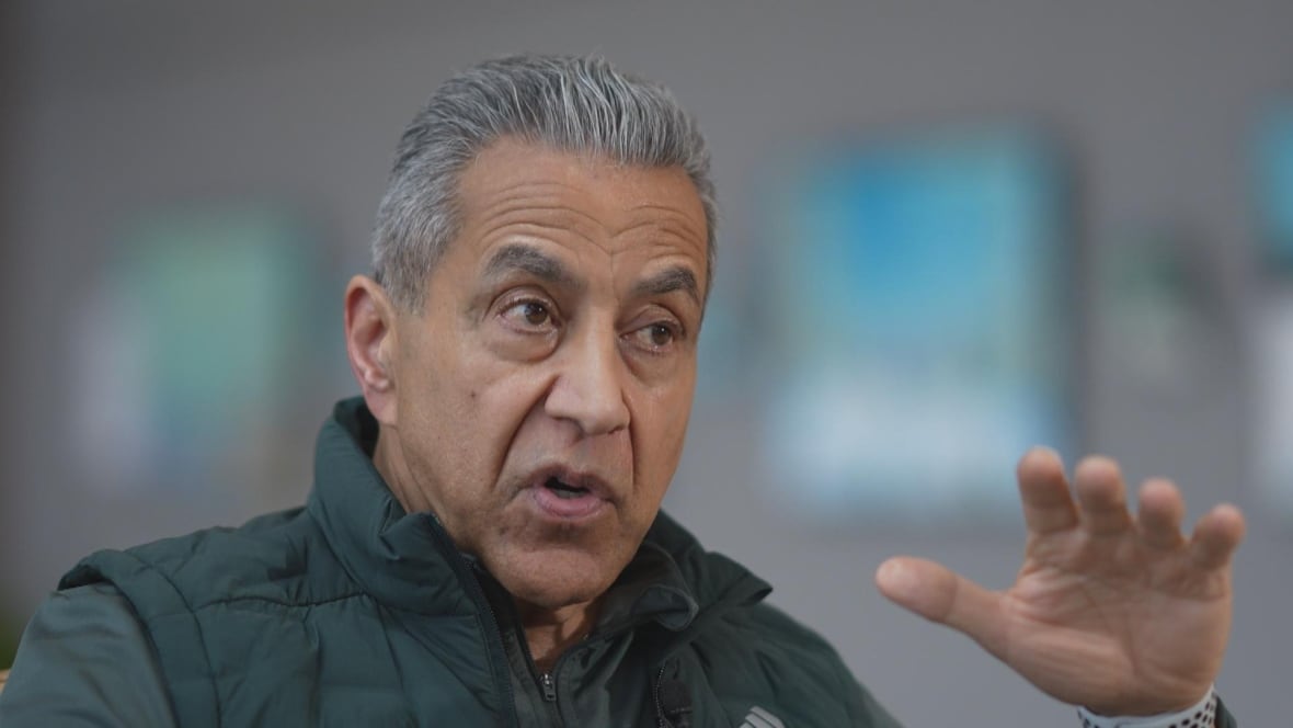 A South Asian man with white hair is seen gesturing as he speaks.