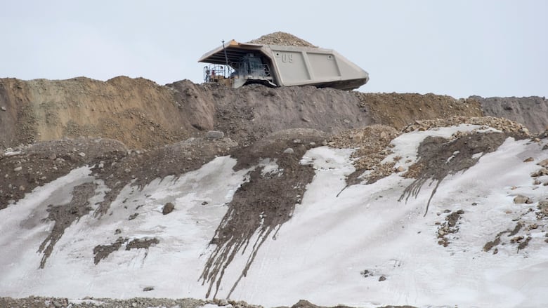 A dump truck drives through a snowy mine site. 