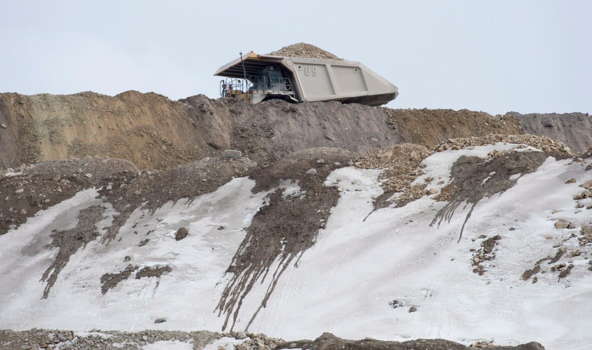 A dump truck drives through a snowy mine site. 