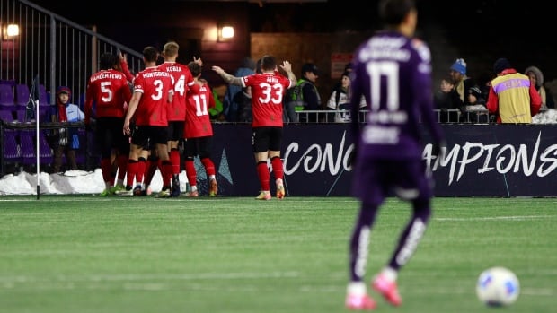 Cavalry FC players celebrate a goal against Pumas UNAM during second half soccer action in round one of the 2025 CONCACAF Champions Cup in Langford, B.C., on Thursday, February 6, 2025. A soccer team is pictured celebrating a goal in the background with a blurred opposition team member pictured in the foreground.