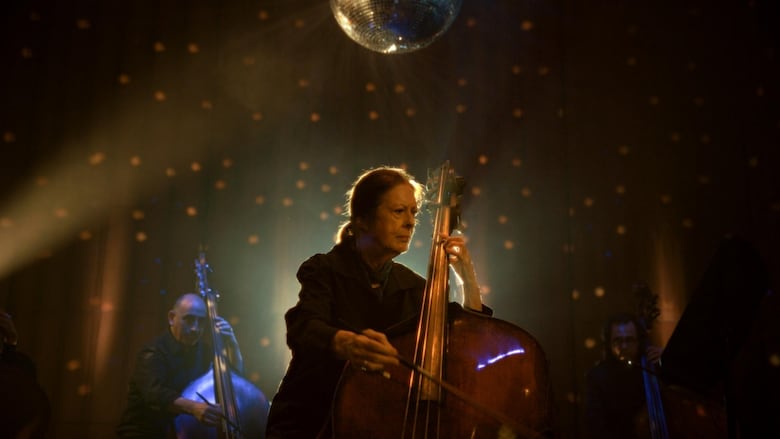 A woman plays the double base on stage surrounded by bright lights