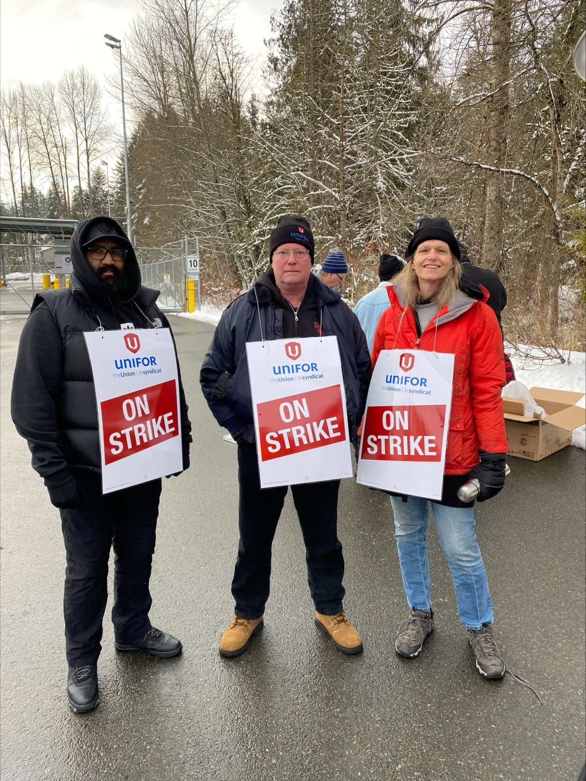 Three workers carry sandwich boards reading 'On Strike' on a snowy day.